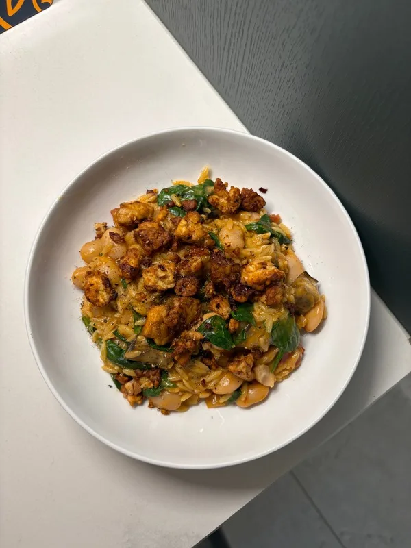 A bowl of creamy orzo with butter beans, spinach and crispy tempeh